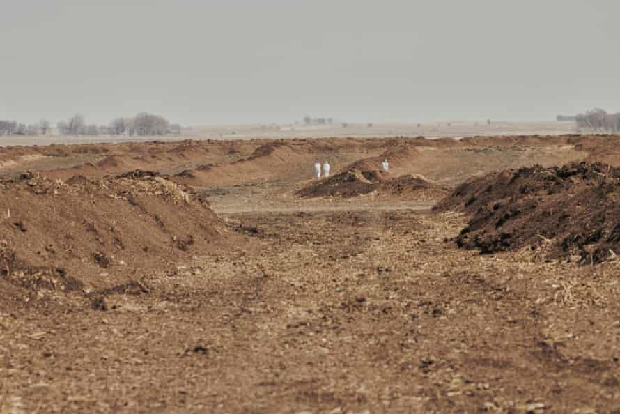 Piles of dirt with small figures in hazmat suits in the background